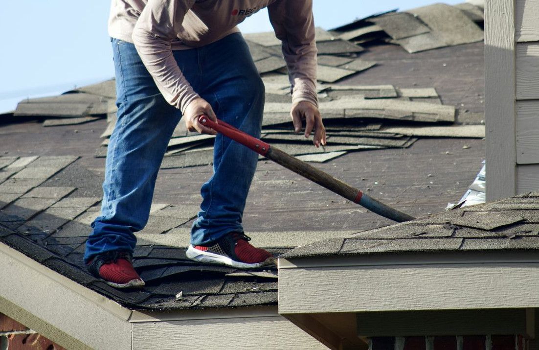 A person in a long-sleeved shirt removing shingles from a residential roof